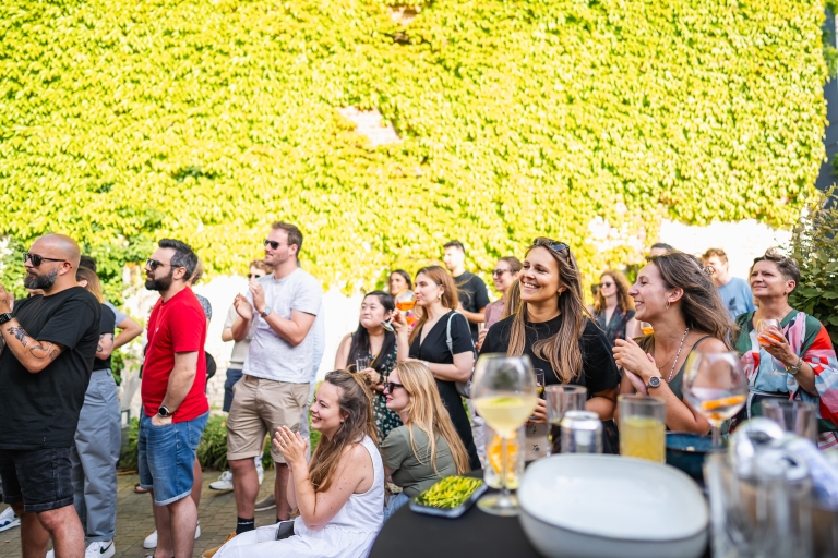 A group of people clapping at Springbok's outdoor summer barbecue in Ghent. They stand before a vibrant green ivy-covered wall, with drinks in hand.